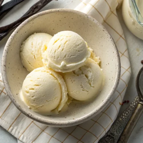 Creamy homemade vanilla ice cream scoops in a rustic ceramic bowl, overhead view, smooth texture visible, surrounded by fresh