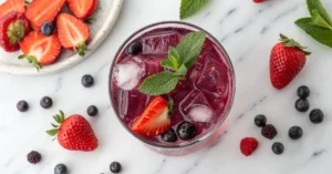Overhead flat lay of a vibrant purple Starbucks Strawberry Acai Refresher copycat drink in a clear glass with ice, fresh stra