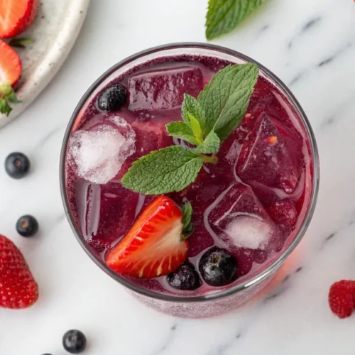 Overhead flat lay of a vibrant purple Starbucks Strawberry Acai Refresher copycat drink in a clear glass with ice, fresh stra